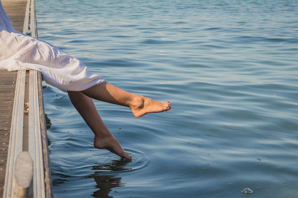 Una mujer joven en un pantalán, balanceando sus pies sobre el agua.