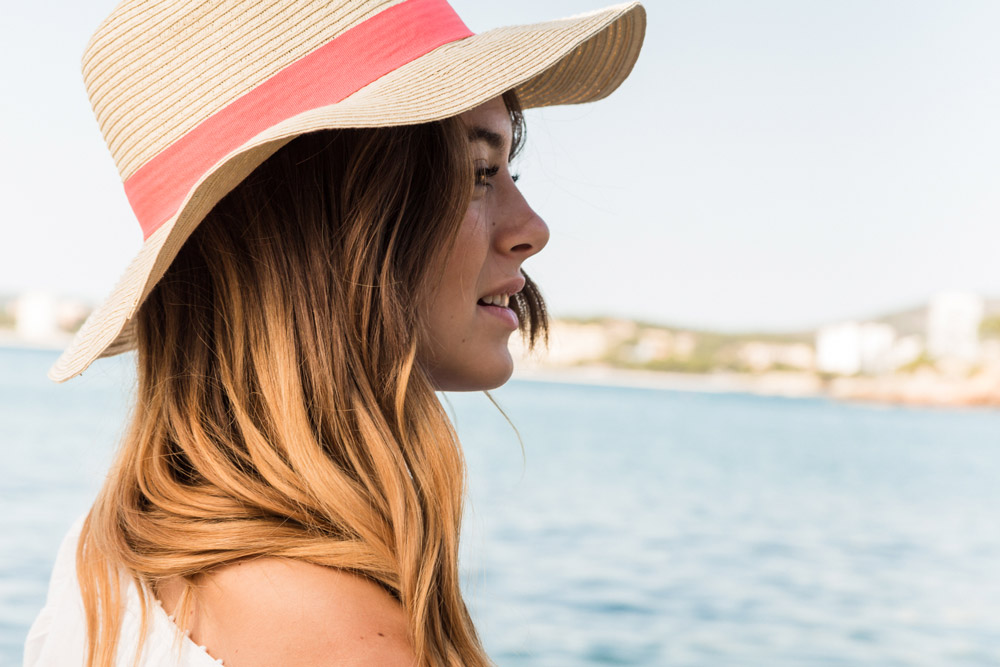 A young woman with beautiful hair is wearing a sun hat, looking to the sea